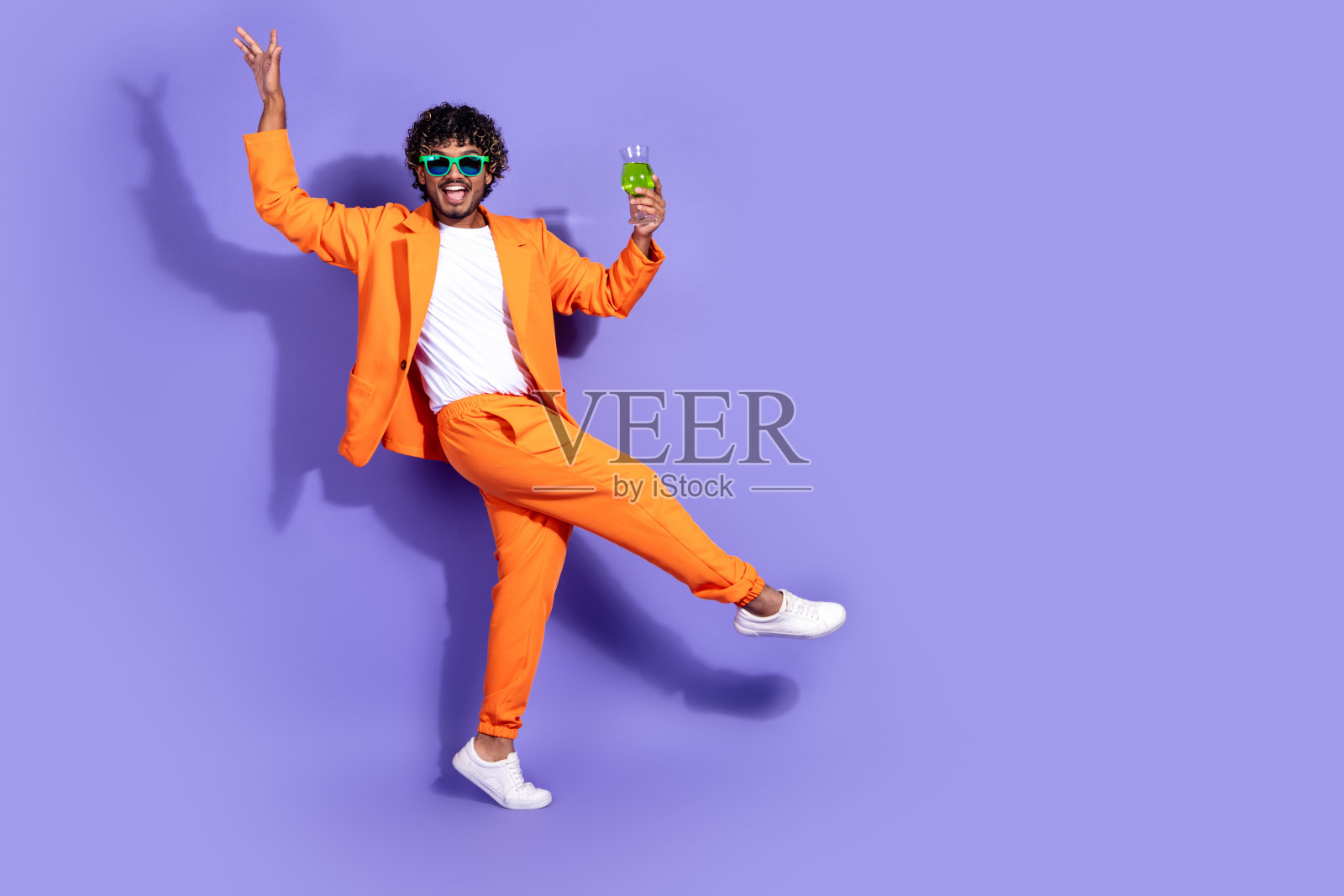 穿着橙色夹克的快乐积极男士在紫色背景下享受饮酒，尽情舞动，周围空旷。照片摄影图片
