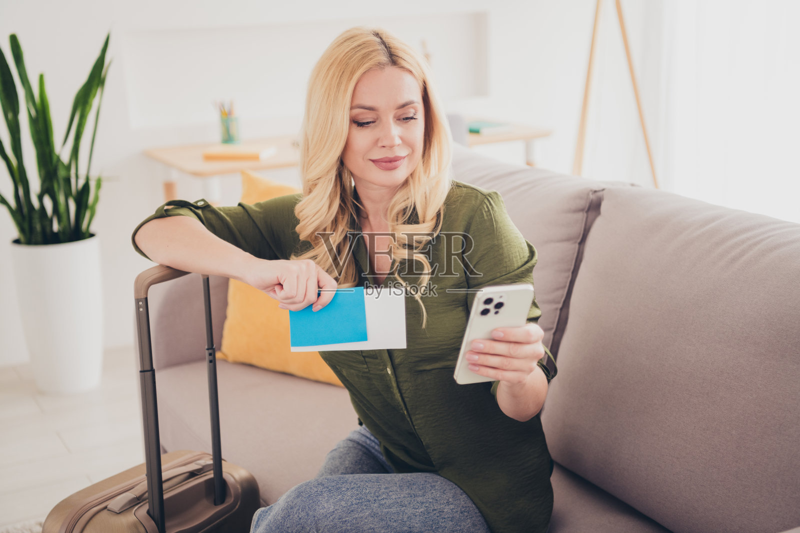 可爱的女人坐在沙发上，手里拿着行李箱，准备周末旅行。照片摄影图片