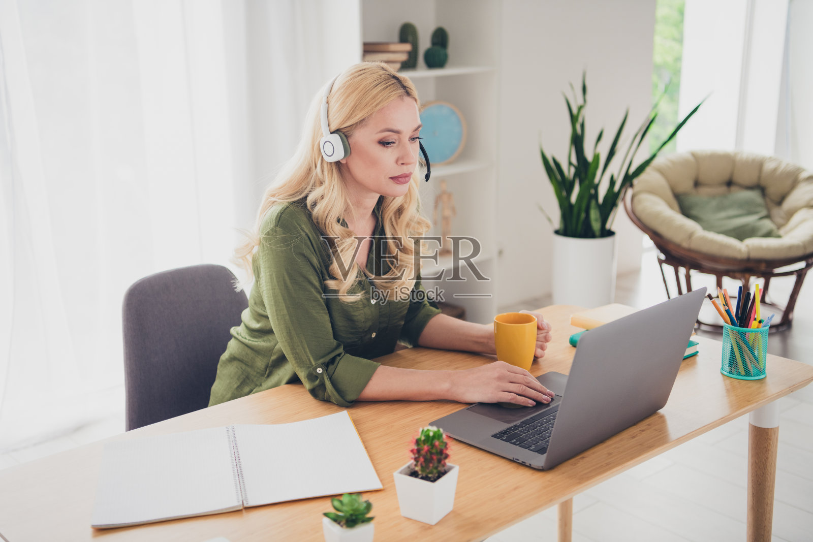 迷人自信的女性顾问坐在家中公寓的桌子旁喝茶，工作于室内。照片摄影图片