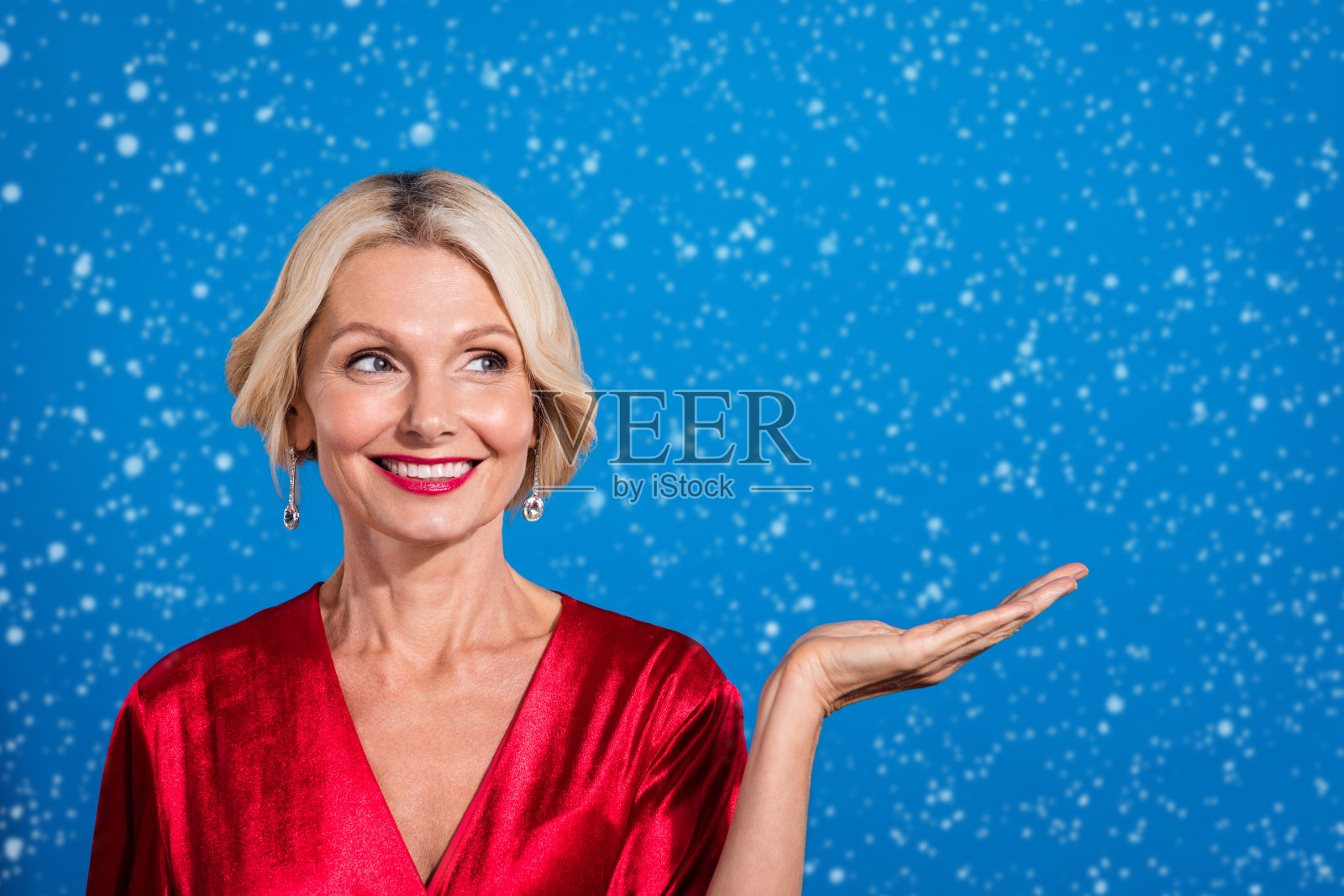迷人梦幻的退休女士穿着闪亮的红色服装，微笑着望向空旷的空间，背景为蓝色。照片摄影图片