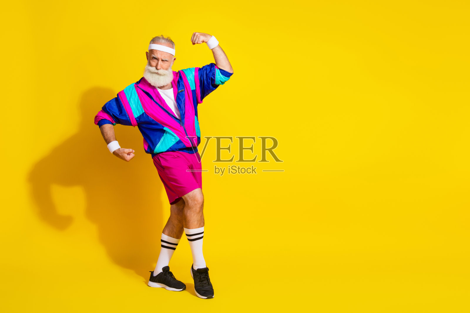全身照，运动风格的时尚现代退休老人，穿着复古夹克，展示肌肉，背景为空旷的黄色。照片摄影图片