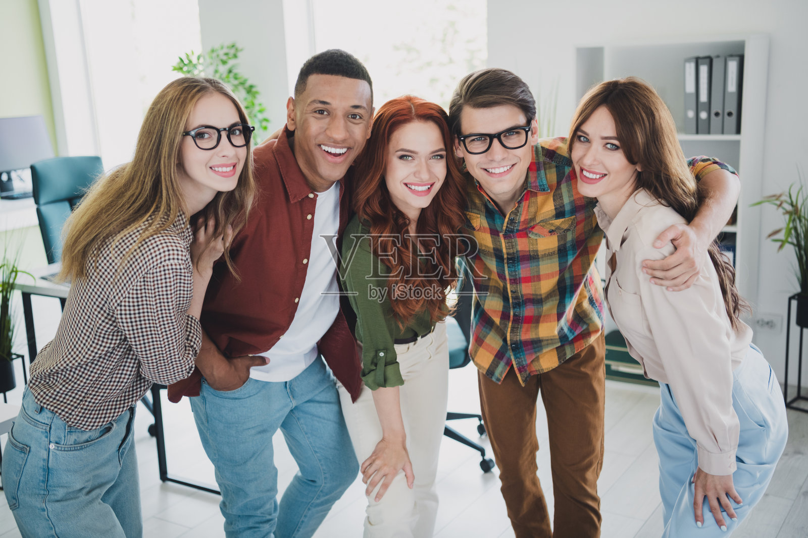 五名年轻的企业员工在办公室商务中心的工作站内微笑拥抱照片摄影图片