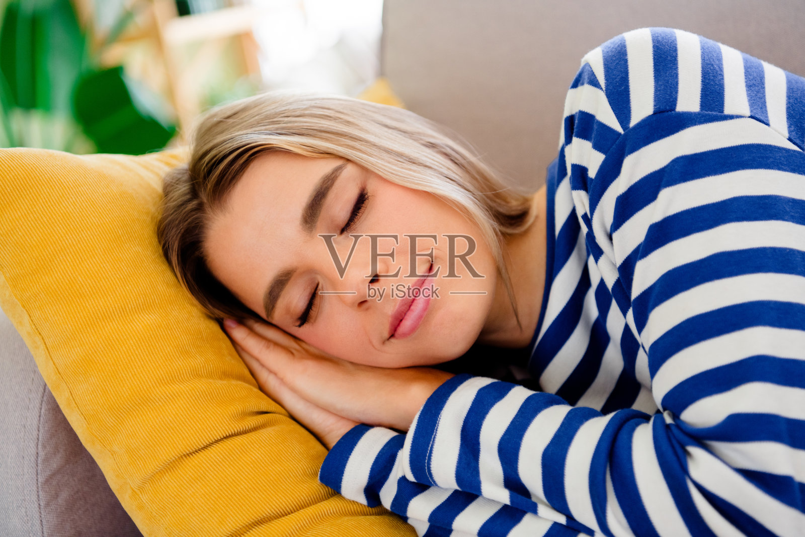 一位迷人的金发年轻女性穿着条纹服装，躺在沙发上睡觉，享受温馨的家庭室内光线。照片摄影图片