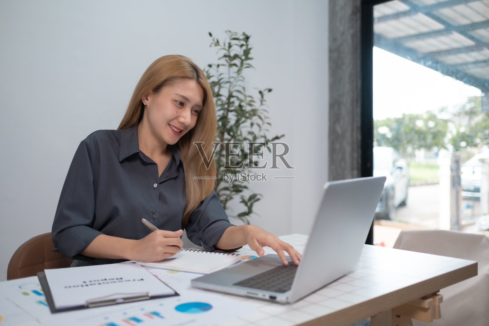 专注的职业女性在家中的客厅使用笔记本电脑，职业女性在办公室使用笔记本电脑阅读财务报告。照片摄影图片