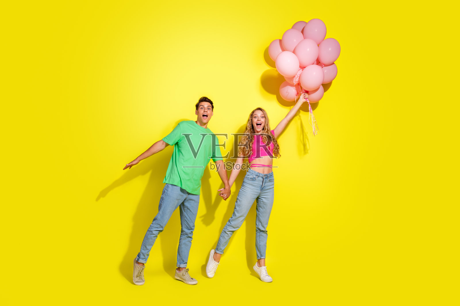 两位年轻的伙伴全身肖像，手持气球，背景为鲜艳的黄色。照片摄影图片