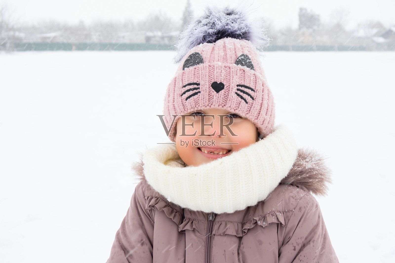 小女孩在雪中玩耍，面带微笑，戴着温暖的冬帽和围巾。照片摄影图片