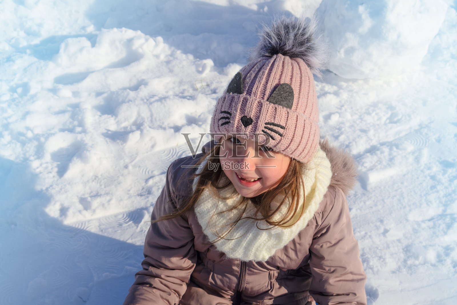 戴着针织帽的小女孩在阳光明媚的冬日雪地里玩耍照片摄影图片