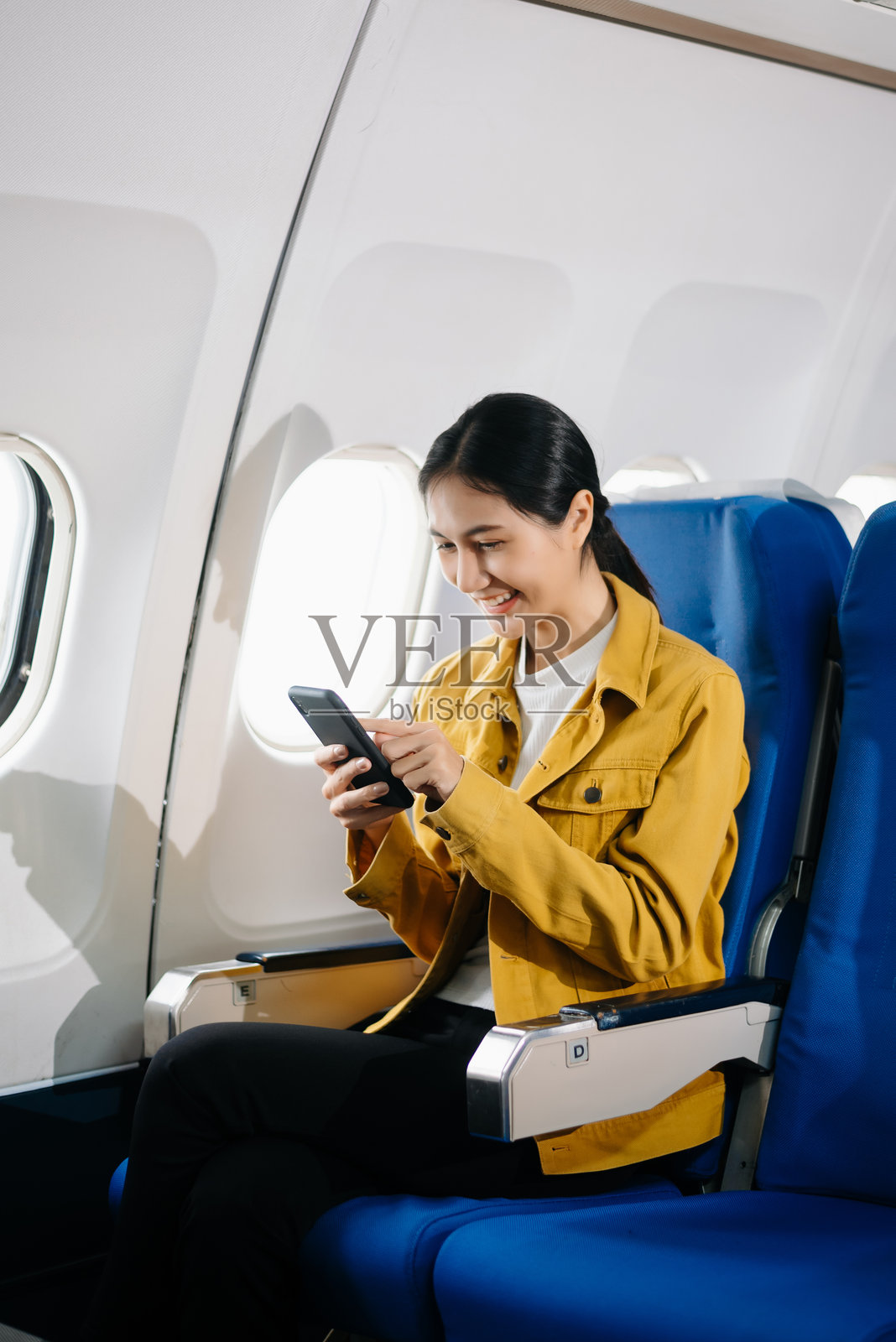 迷人的亚洲女性乘客坐在舒适的飞机座位上，一边使用笔记本电脑和平板电脑工作。优雅地旅行，优雅地工作。照片摄影图片