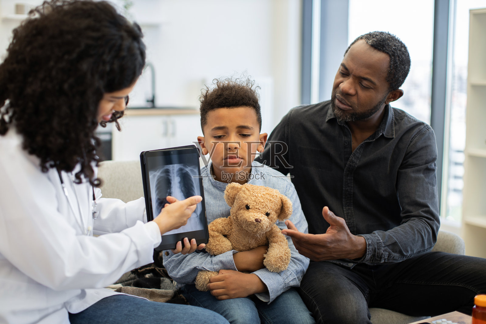 医生向担心的男孩和父亲展示肺部X光片的平板电脑照片摄影图片