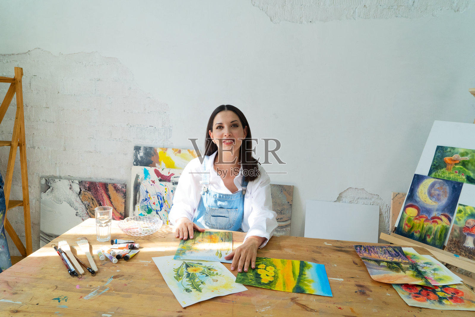 一位快乐的艺术家自豪地展示着他们五彩缤纷的画笔，置身于一个明亮而富有启发性的工作室环境中。照片摄影图片