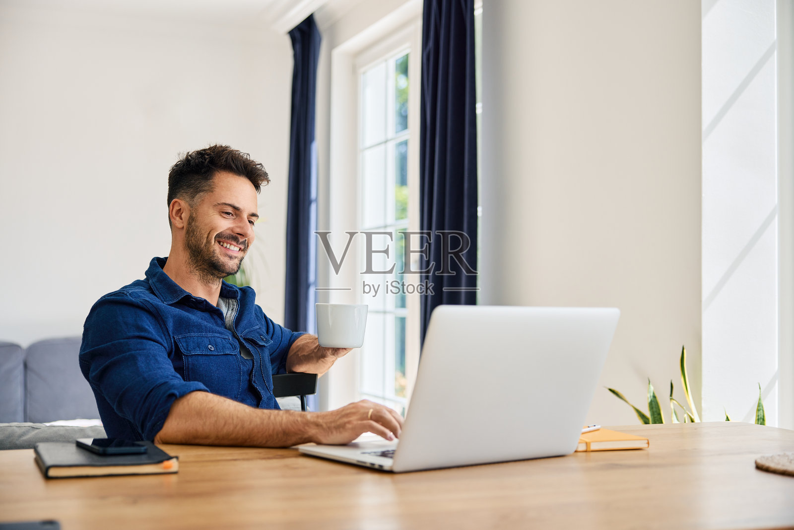 无忧无虑的男人在家中坐在桌旁使用笔记本电脑远程工作照片摄影图片