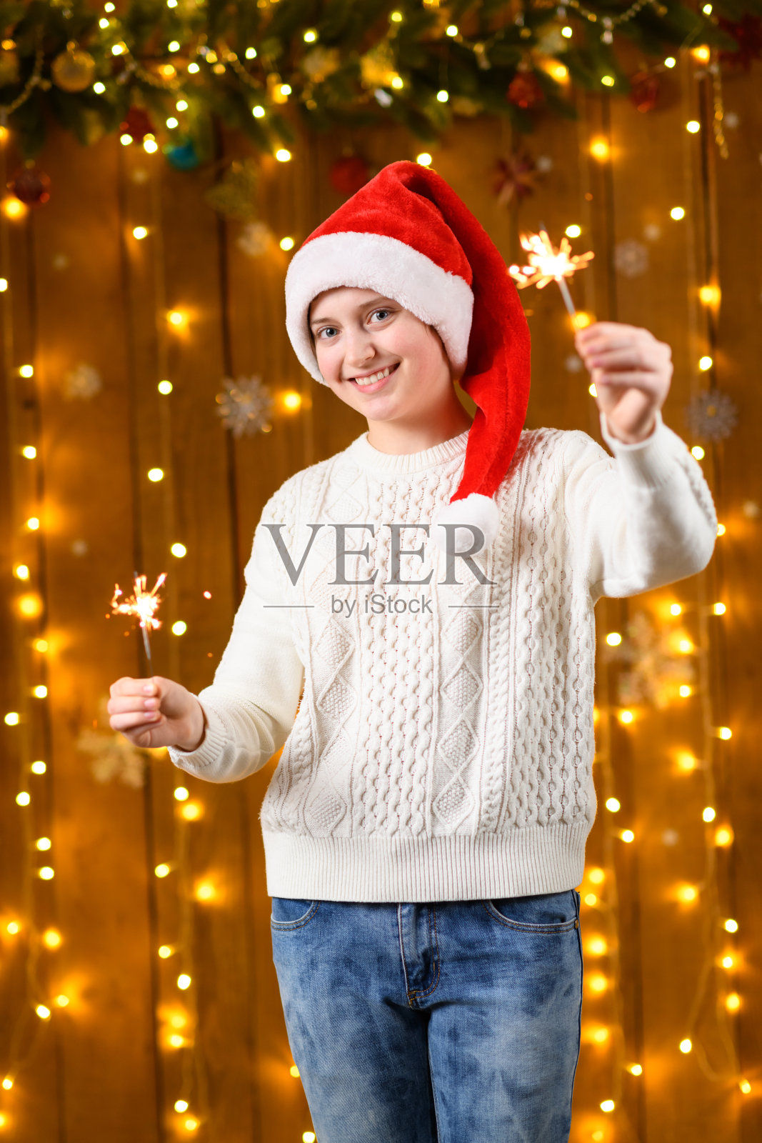 一个少女手持烟花棒，身边是新年节日装饰、节日灯光和花环。照片摄影图片