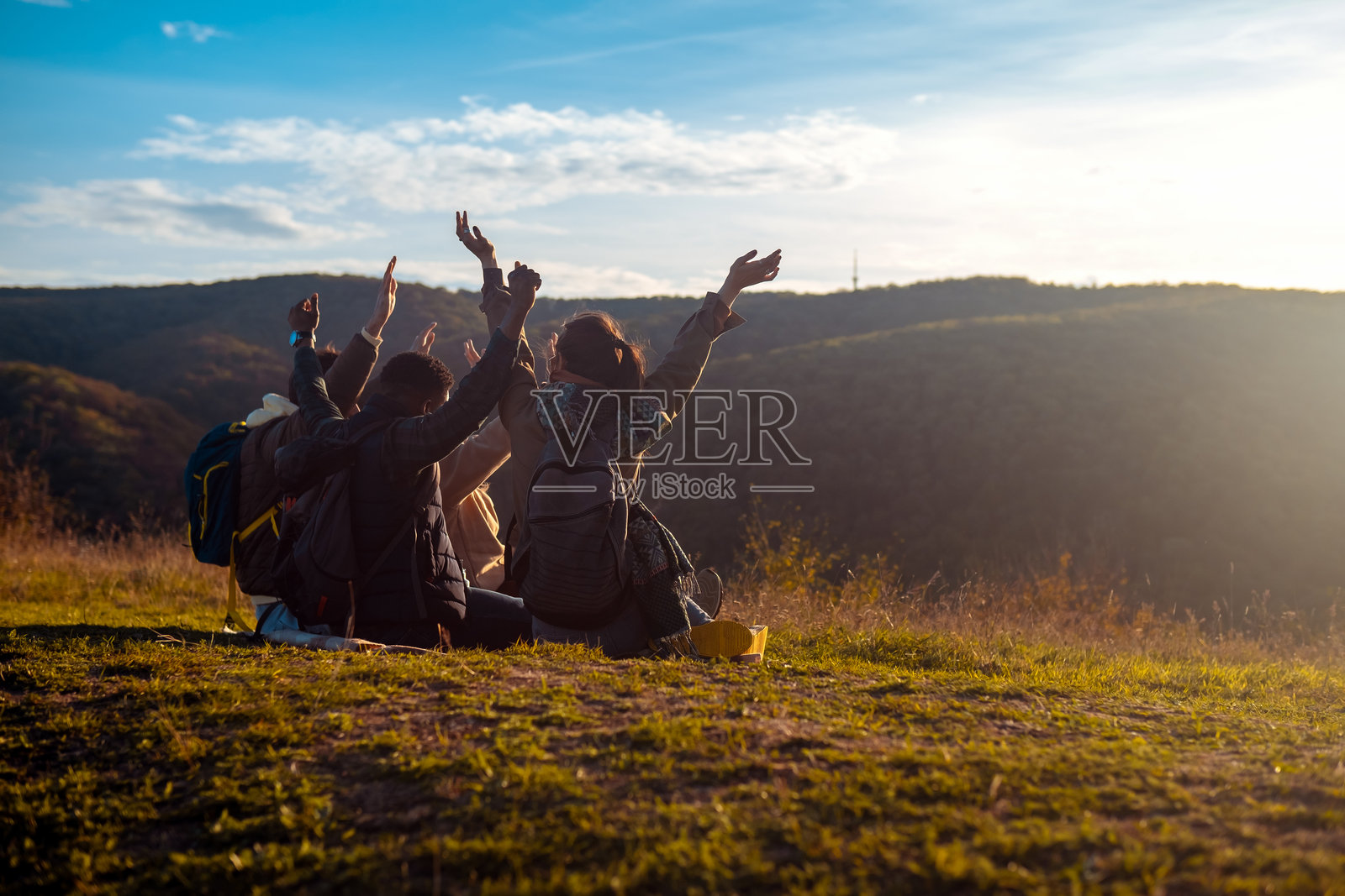 一群朋友坐在山顶上休息，背对着镜头，欣赏日落。照片摄影图片