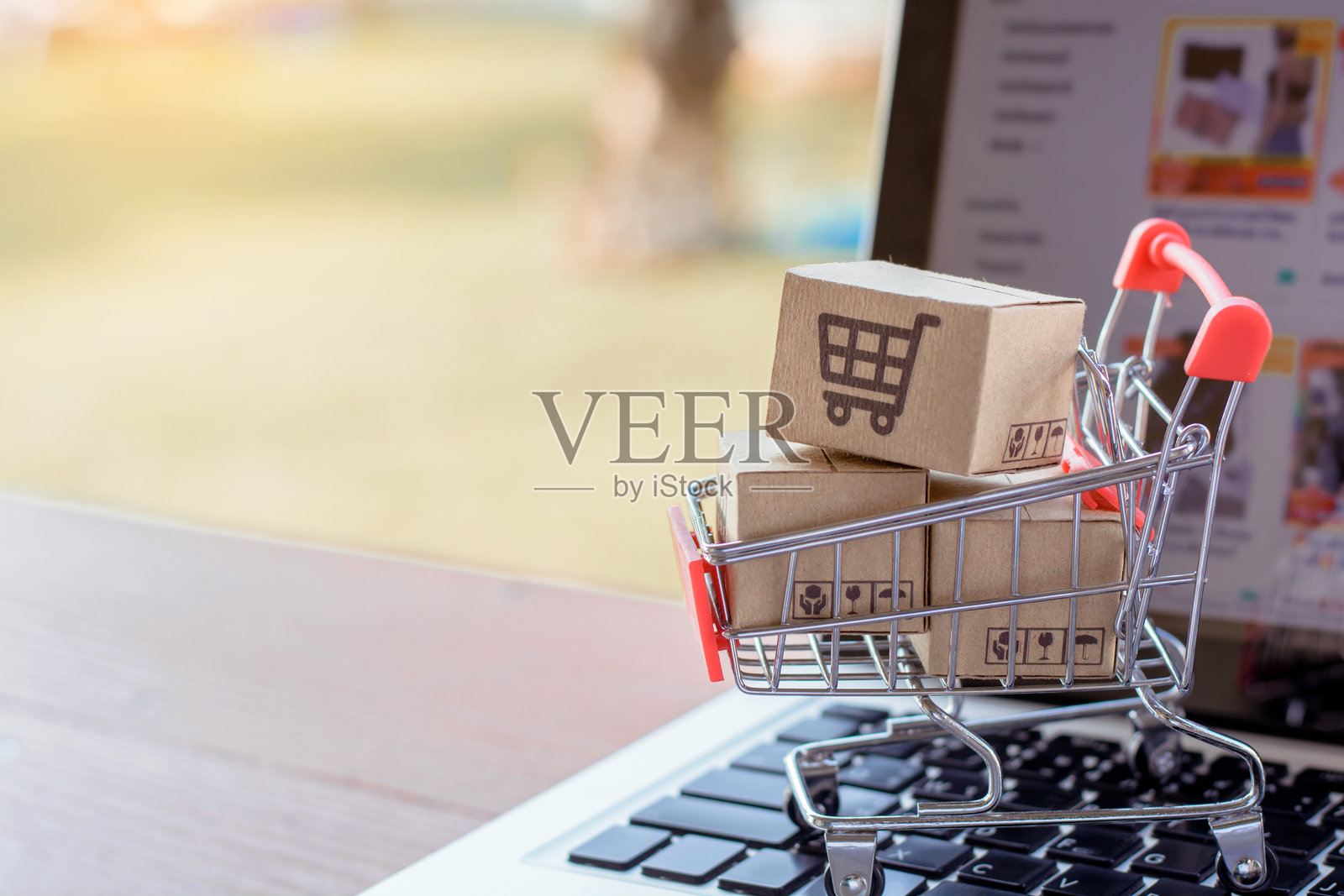 在线购物。笔记本电脑键盘上放着一个带购物车标志的纸箱。网络购物服务，提供送货上门。照片摄影图片