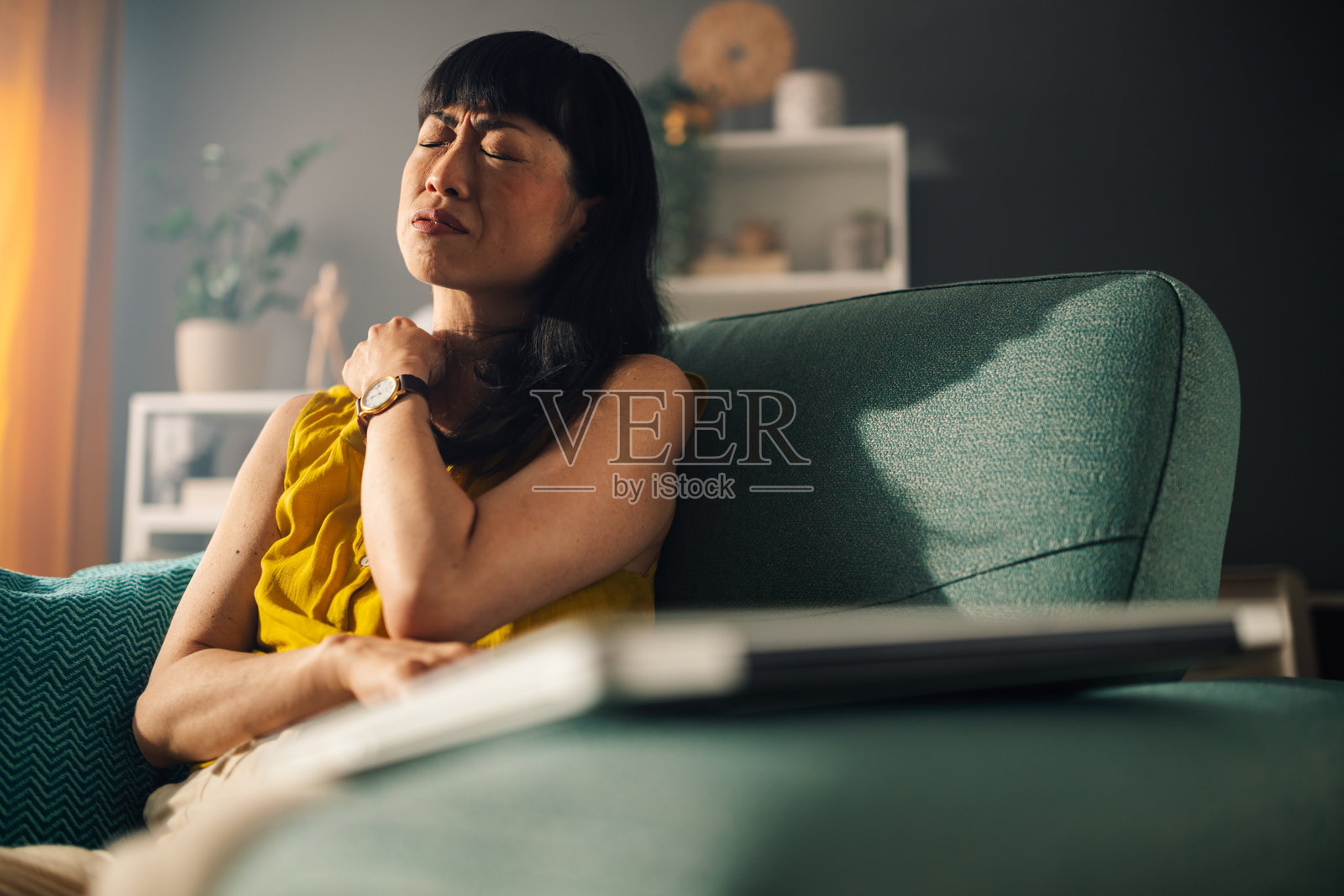 穿着黄色上衣的亚洲女性舒适地靠在青色扶手椅上。照片摄影图片