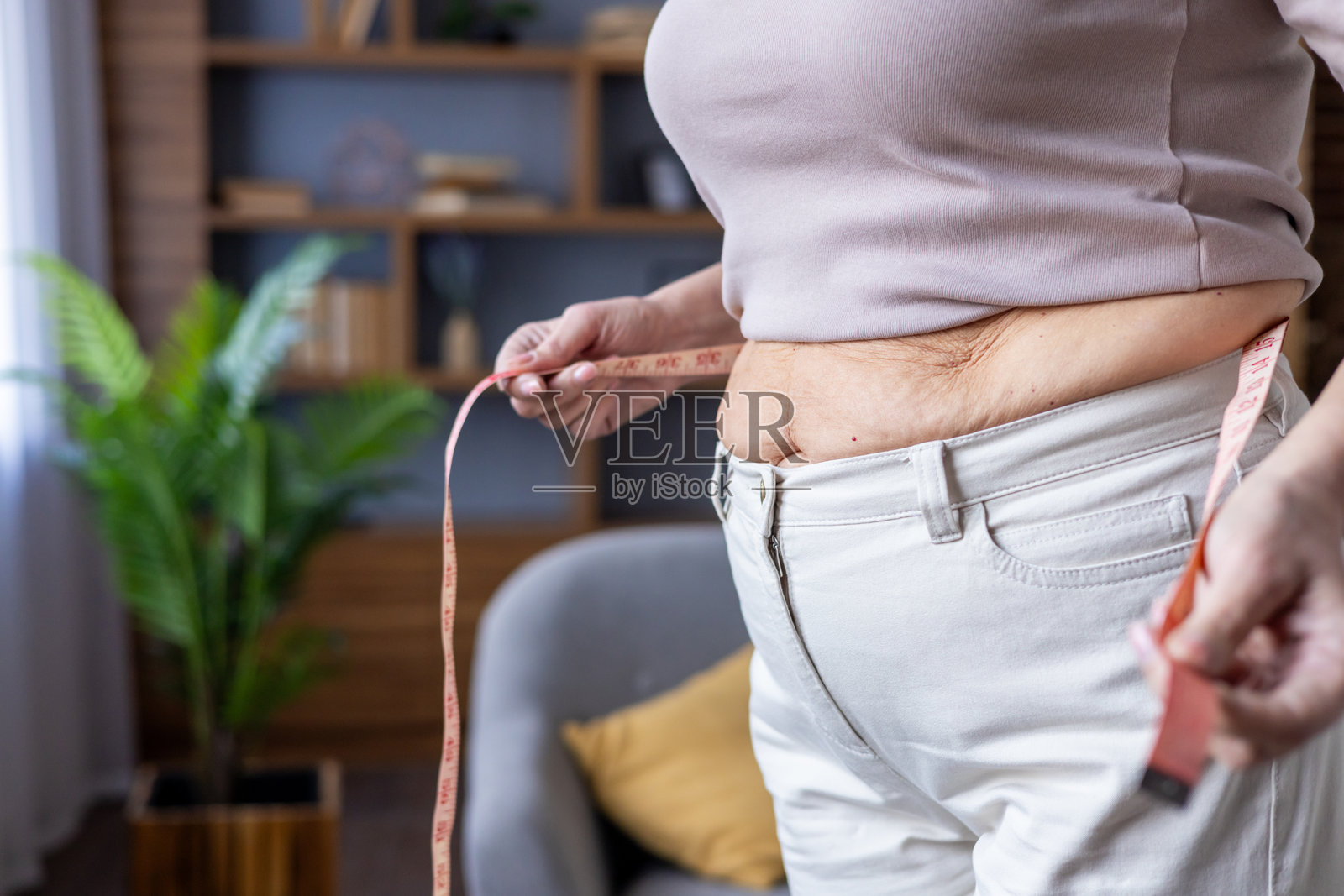 女性在家中用卷尺测量自己的腰围，专注于身体积极性和个人健身目标。照片摄影图片