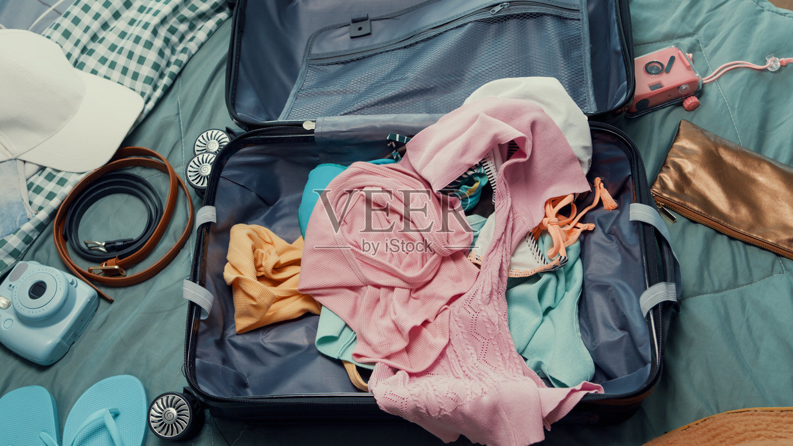 俯视图。年轻快乐兴奋的亚洲女性在卧室准备行李箱，往包里塞衣物和配饰，为夏季假期做准备。照片摄影图片