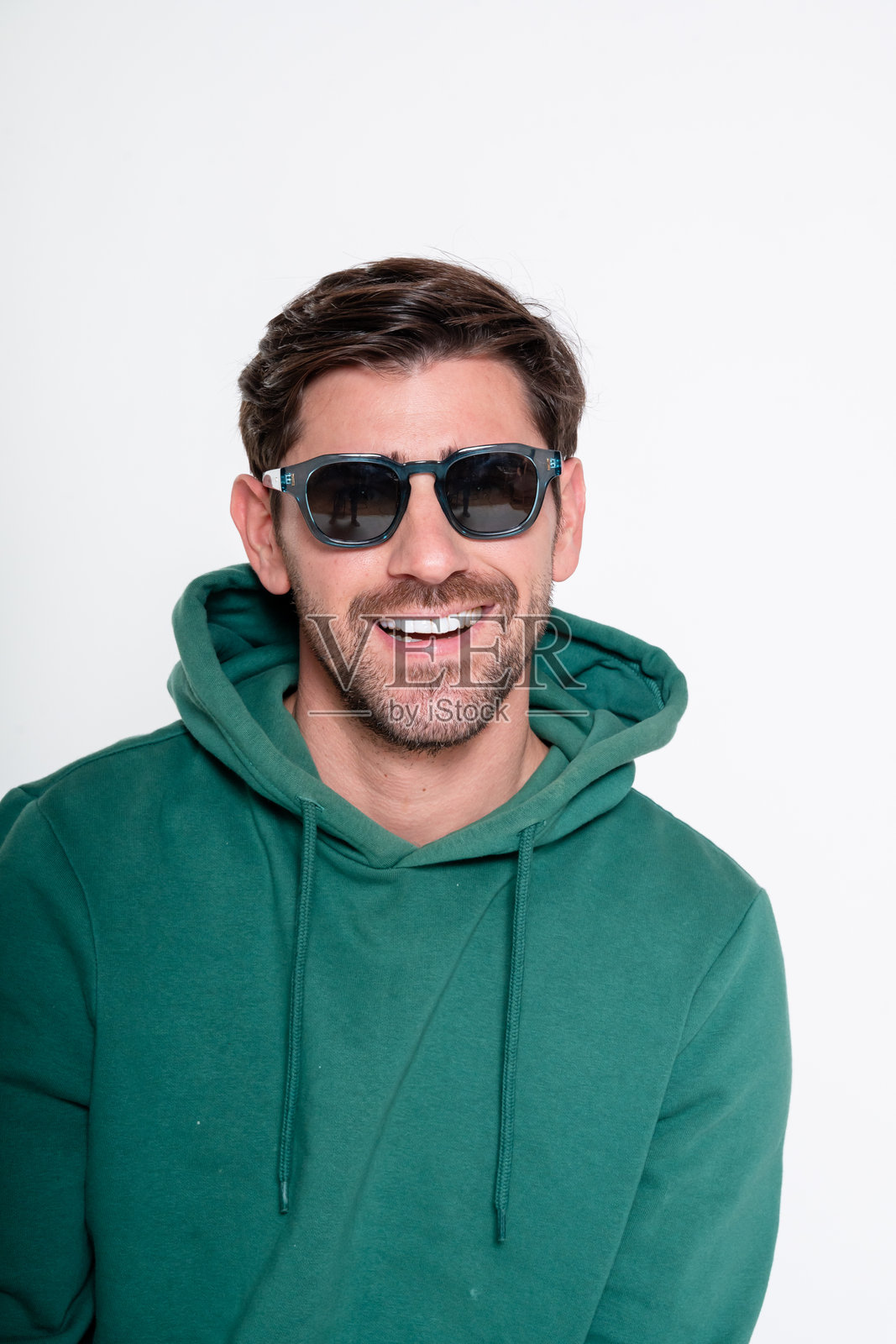 微笑的男子穿着太阳镜和绿色连帽衫在摄影棚中摆姿势照片摄影图片