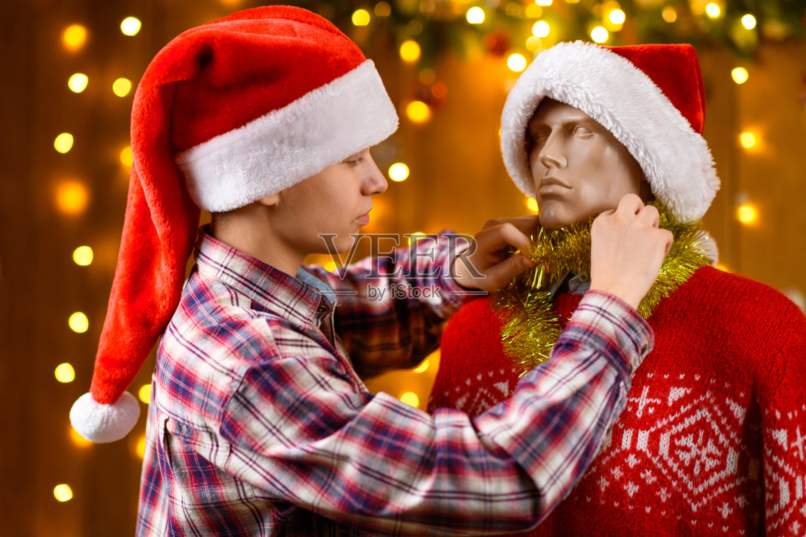 一个少年与一个男性人偶摆姿势，作为朋友，身边是新年装饰，节日的灯光和花环，圣诞灯饰和装饰，节日主题。照片摄影图片