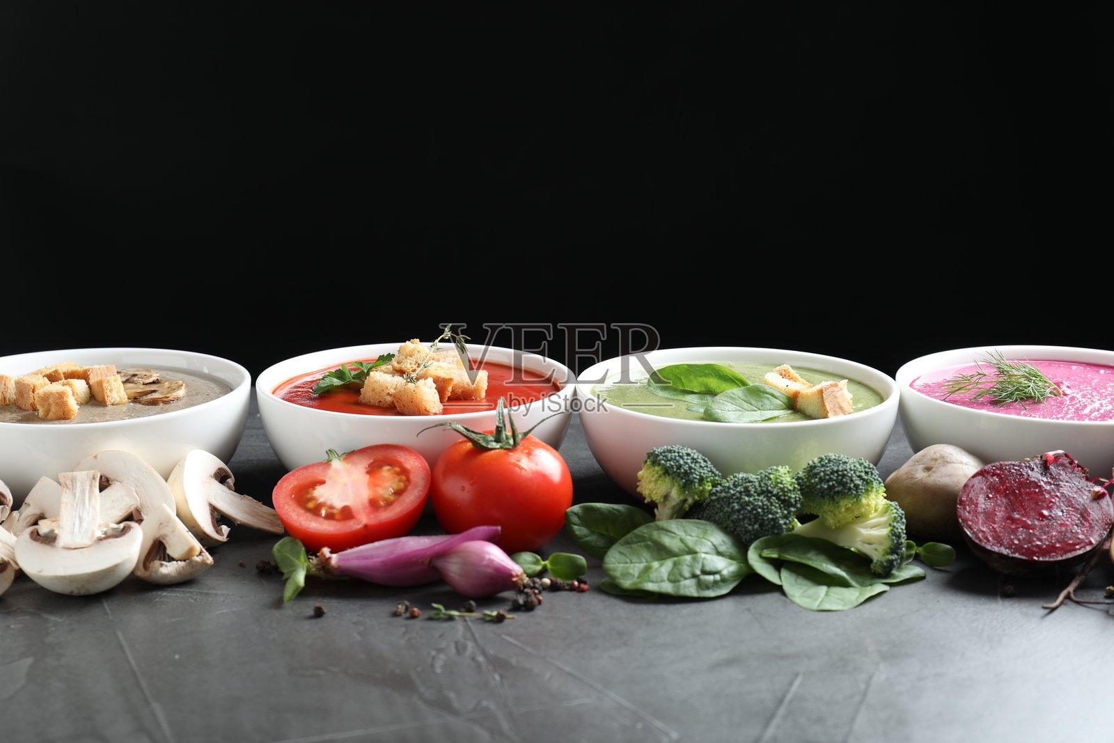 不同口味的奶油汤盛在碗中，配料摆放在深灰色桌面上照片摄影图片