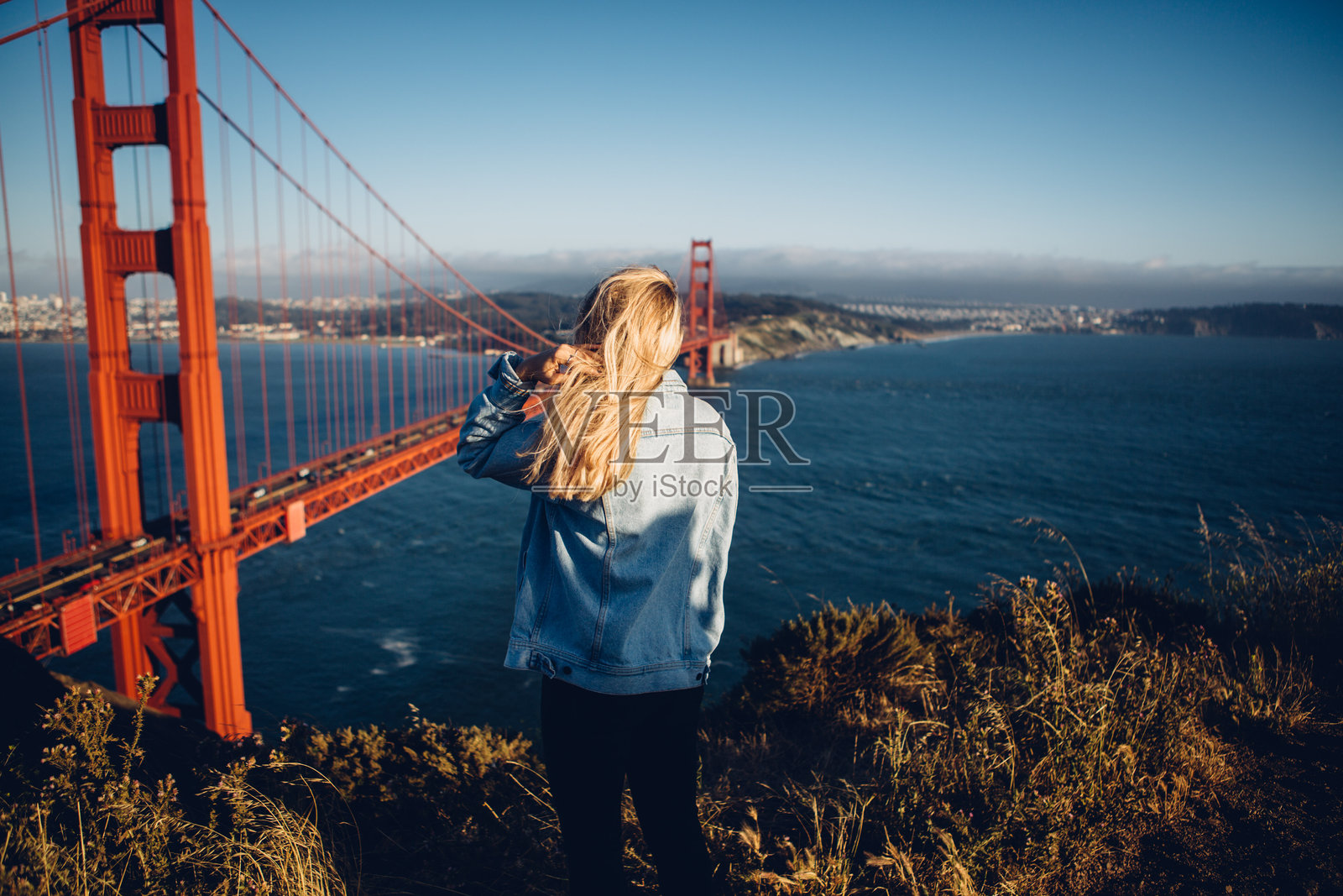 背影的女人站在悬索桥旁，仰望天空照片摄影图片
