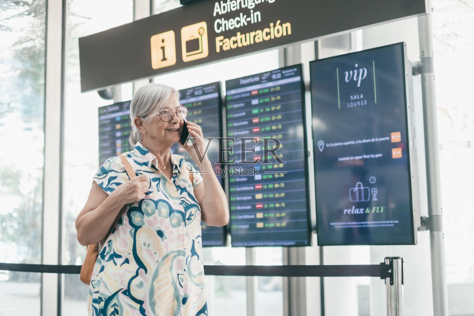 一位年长女性在机场背着背包走向登机口。她正在手机上通话，快乐的旅行者享受着旅行和假期。照片摄影图片