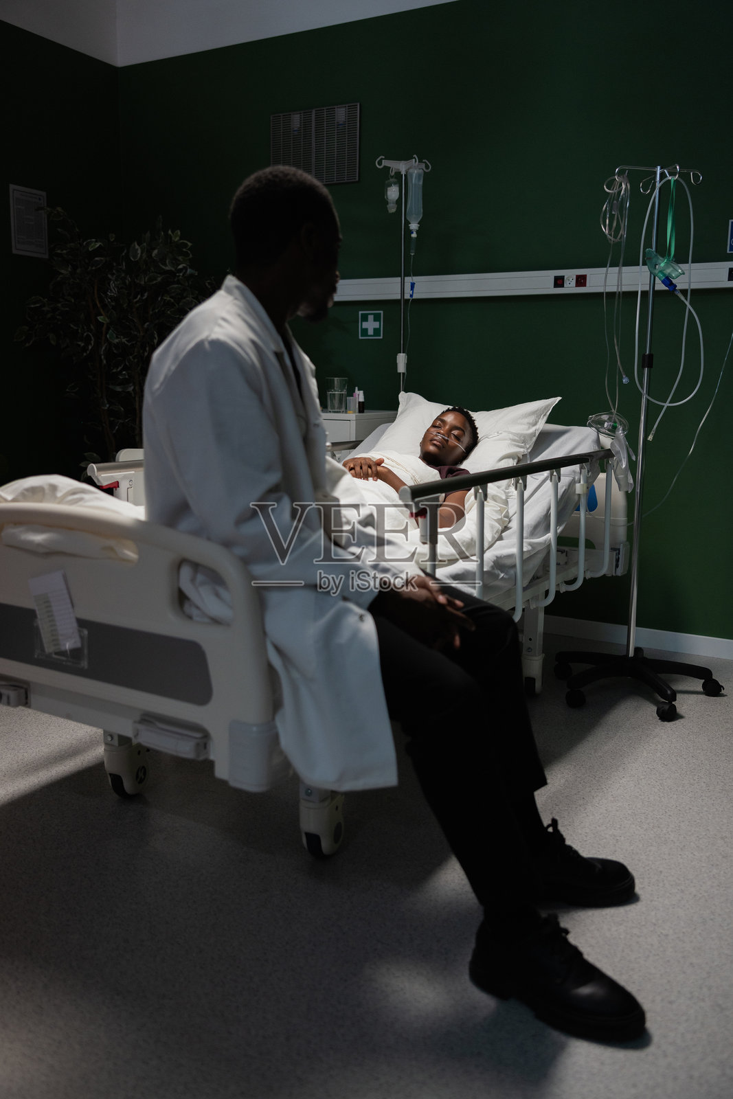年轻的非洲患者在医院病床上休息，氧气管已连接，身边坐着一位关心的医生。照片摄影图片