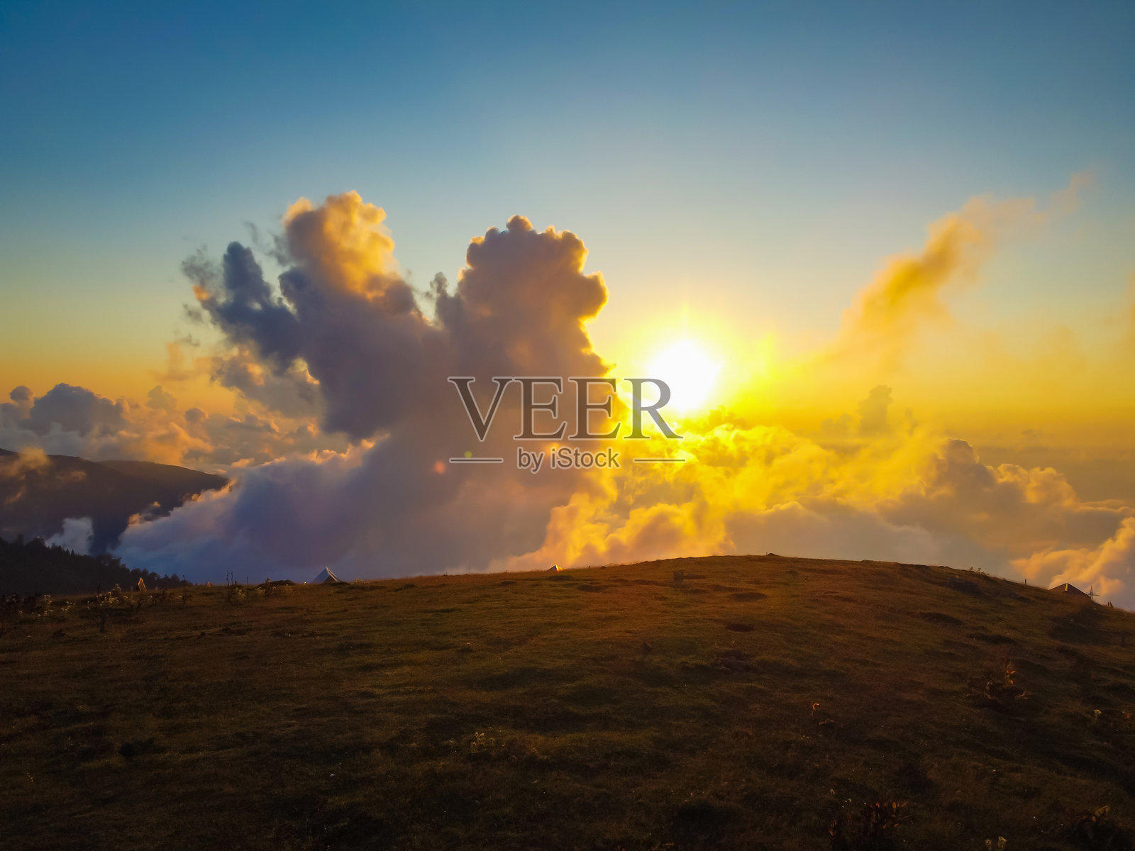 落日将温暖的光线洒在云朵上，投射出长长的阴影覆盖在山间草甸上，天空从白昼过渡到夜晚，给风景涂上金色的橙色和黄色。照片摄影图片