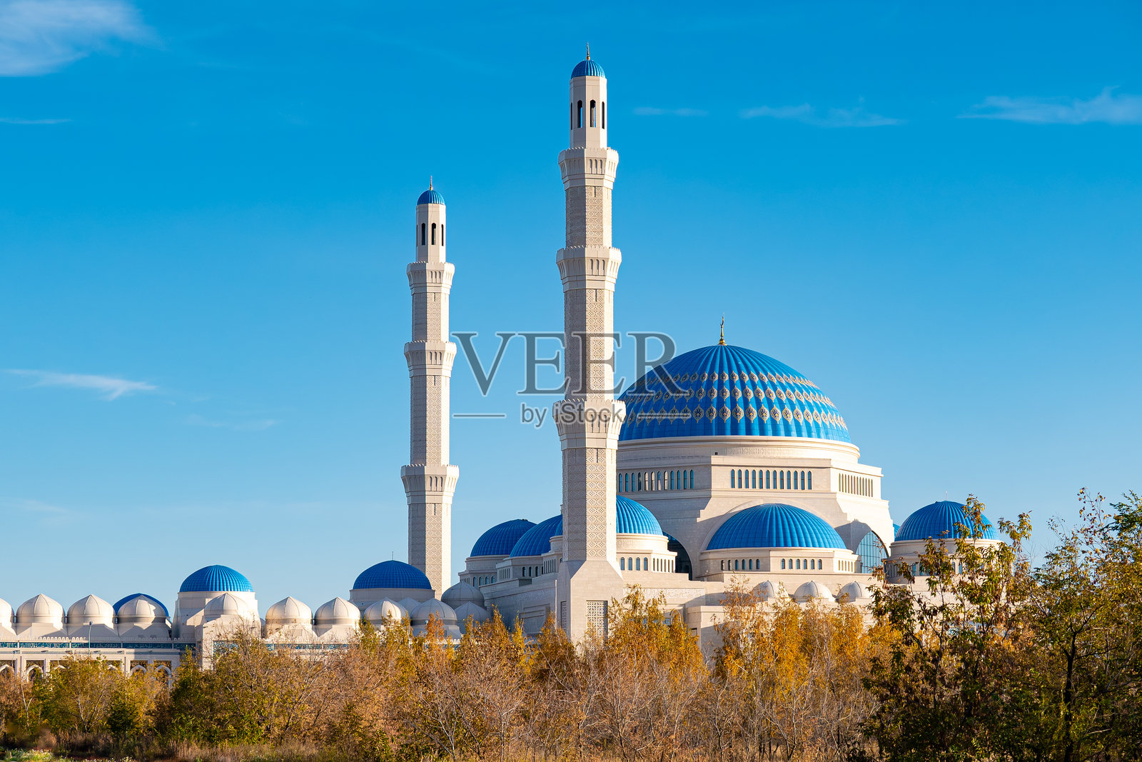 阿斯塔纳的主要中央清真寺，蓝色圆顶和高耸的白色宣礼塔，位于晴朗的蓝天下，四周环绕着秋季景观中的树木。哈萨克斯坦照片摄影图片