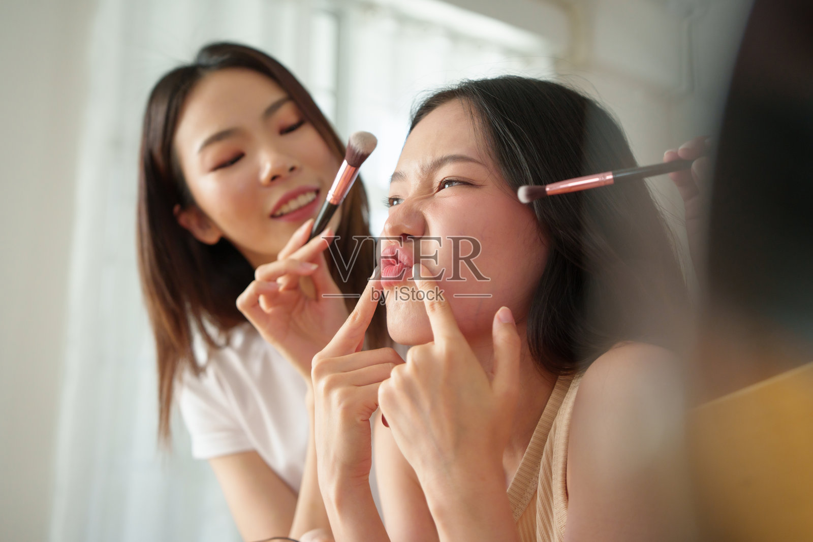 两位年轻的亚洲女性在玩耍中化妆，青少年女孩微笑并做出搞笑表情，捕捉友谊与美丽的瞬间。照片摄影图片