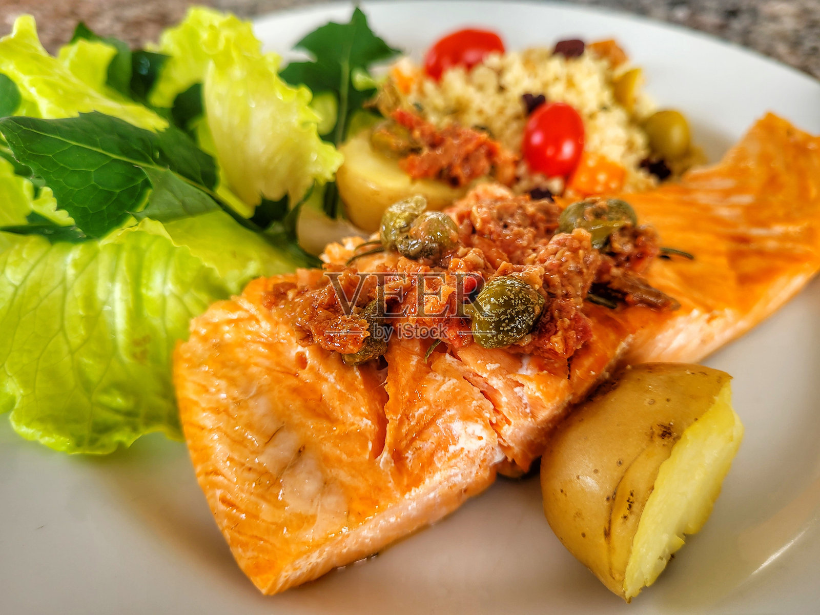 用盐、柠檬和香料调味的三文鱼在新鲜香草上煎制，配有土豆球、库斯库斯、红香蒜酱、刺菜和生菜。照片摄影图片