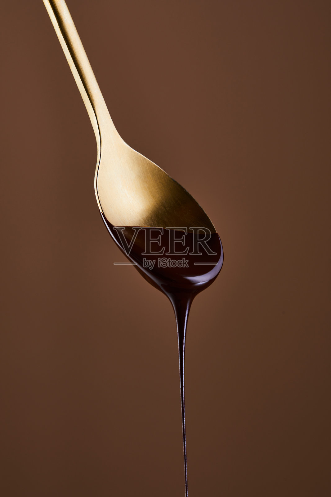 金属勺尖上悬挂着一滴巧克力糖浆照片摄影图片