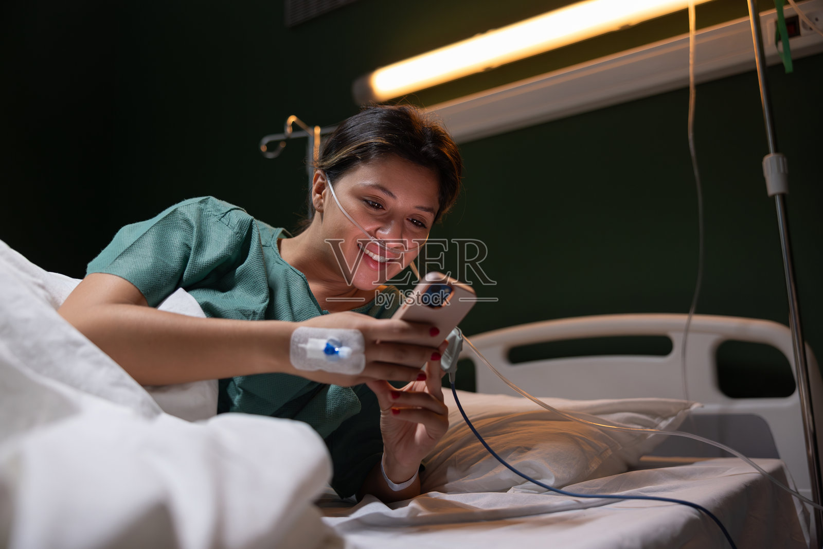 一位美丽的年轻女孩在医院因重感冒接受治疗，手中拿着手机与家人进行群聊。照片摄影图片