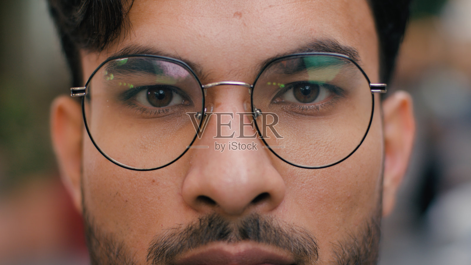 特写镜头，冷静、自信、放松的印度阿拉伯裔男性学生、客户、商人模特，戴着眼镜，睁开美丽的棕色眼睛，注视着镜头，背景为城市街道。眼科学照片摄影图片