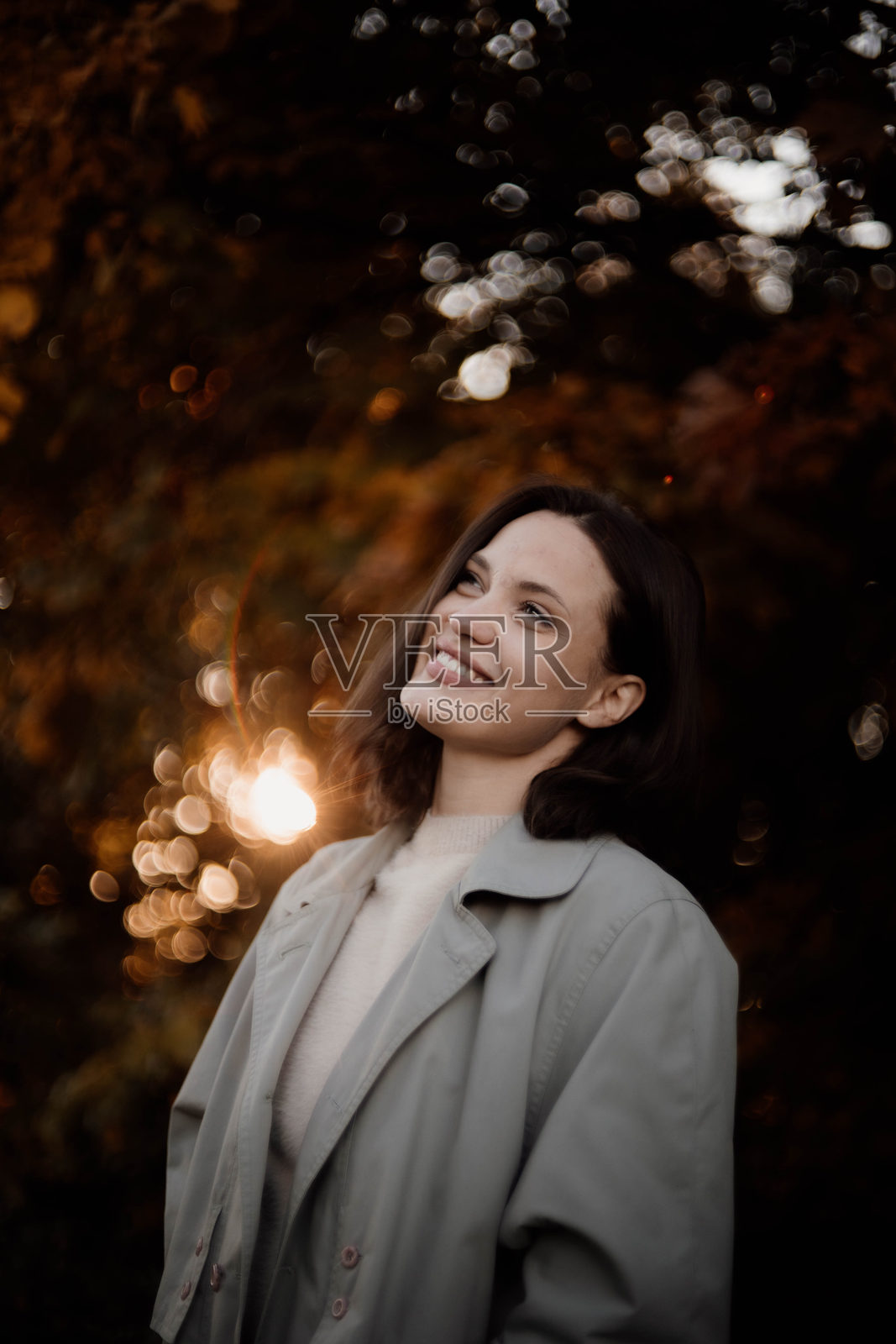 穿着秋季外套的女性在森林中享受秋天的风景，树上黄叶飘落。照片摄影图片