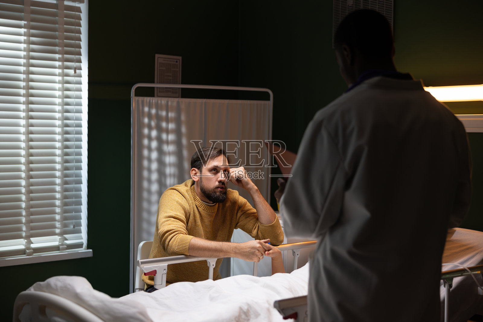 在医院里，一名男子在昏迷的女友身边与医生交谈，女友刚经历了一场严重的事故。照片摄影图片