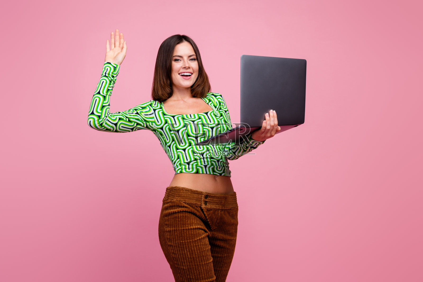 可爱的快乐女性穿着时尚的绿色衣服，手持小工具，背景为粉色。照片摄影图片