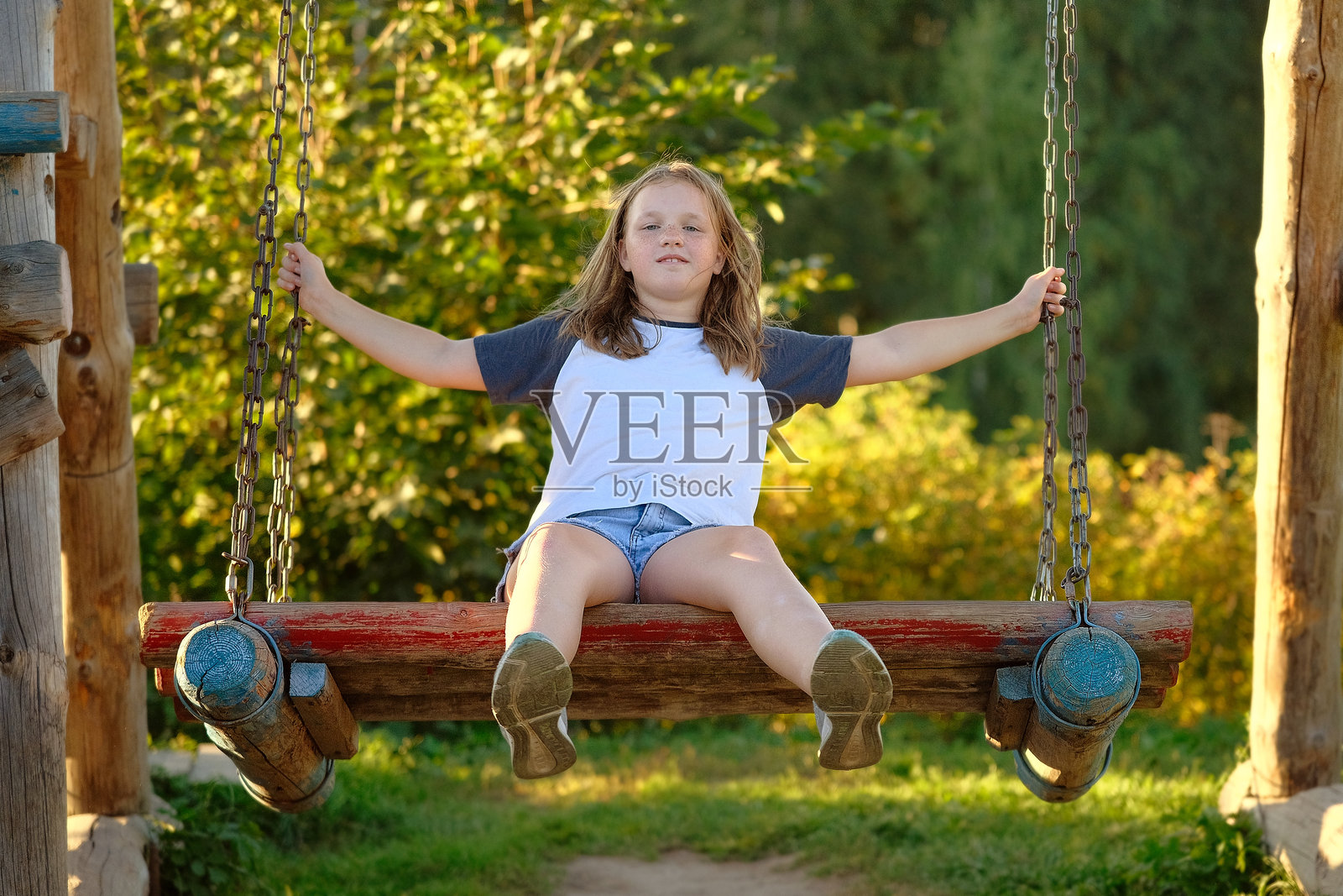 快乐的女孩在秋千上。孩子在游乐场的大木制跷跷板上荡秋千。照片摄影图片