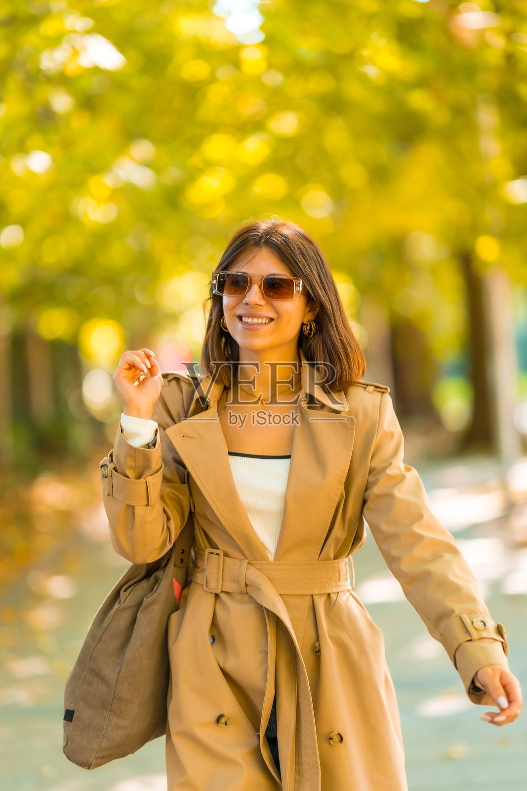 一位穿着浅棕色风衣和太阳镜的女性走在人行道上照片摄影图片