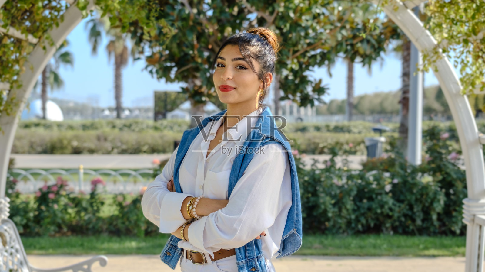 一位年轻的棕发女商人在春天的公园里微笑着看向镜头，周围是满树的绿意。照片摄影图片