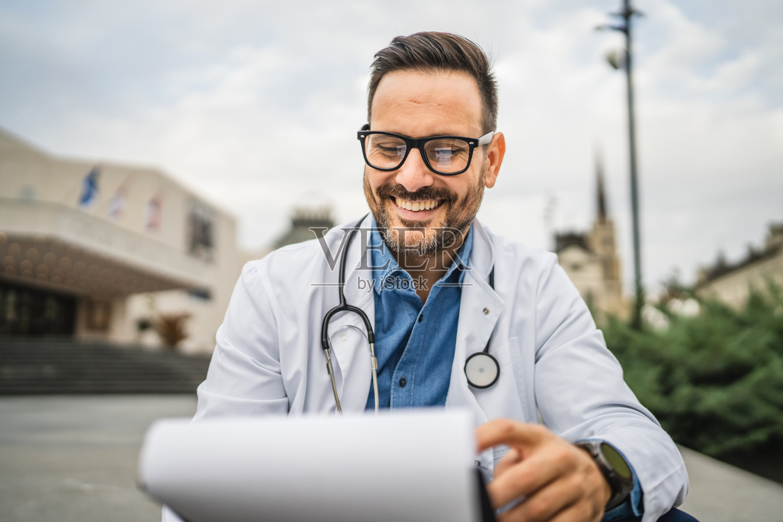 成年男性医生坐在诊所前，查看夹板上的信息。照片摄影图片