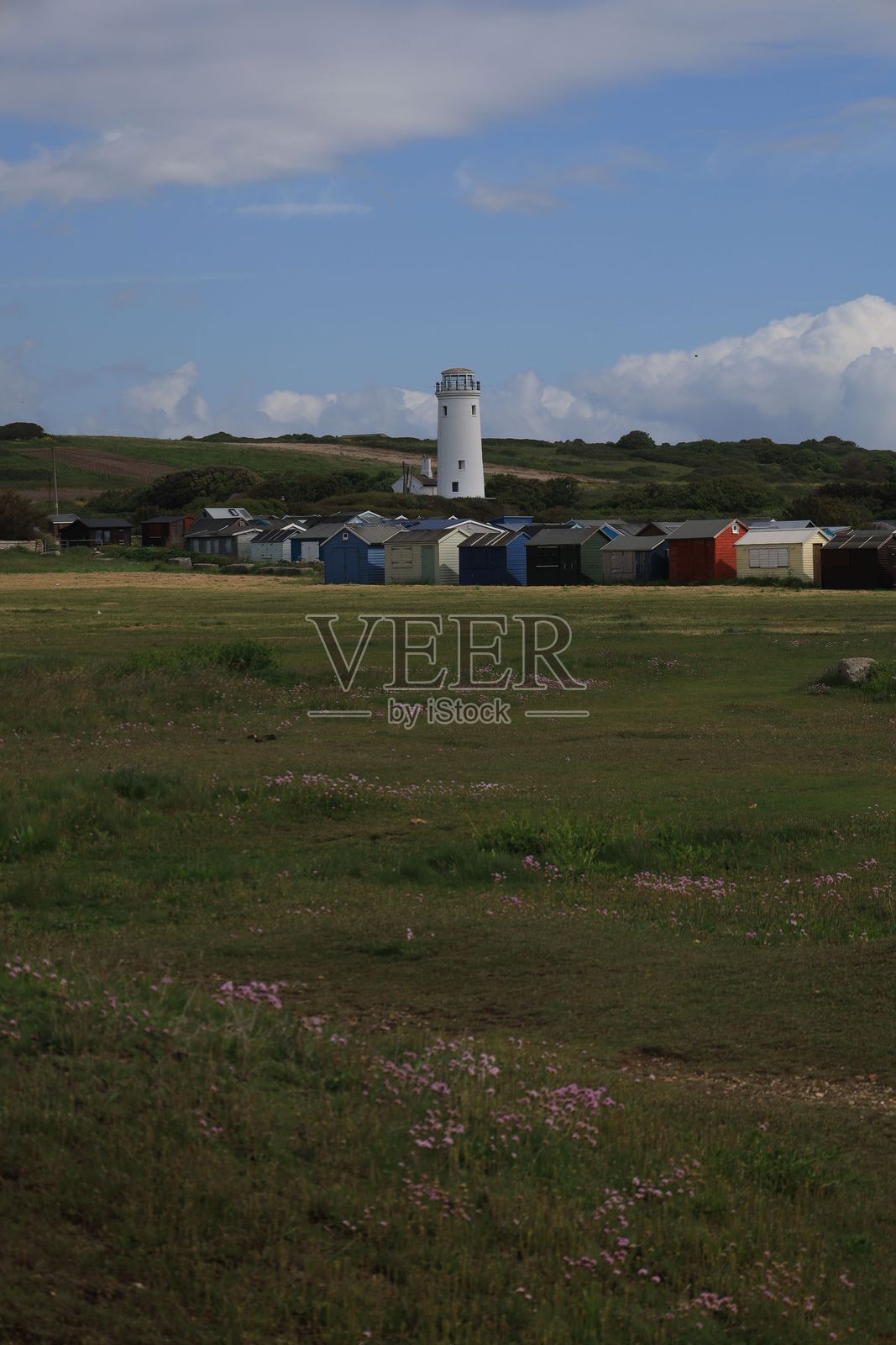 白色灯塔矗立在山丘上，俯瞰着一片五彩斑斓的海滩小屋。照片摄影图片
