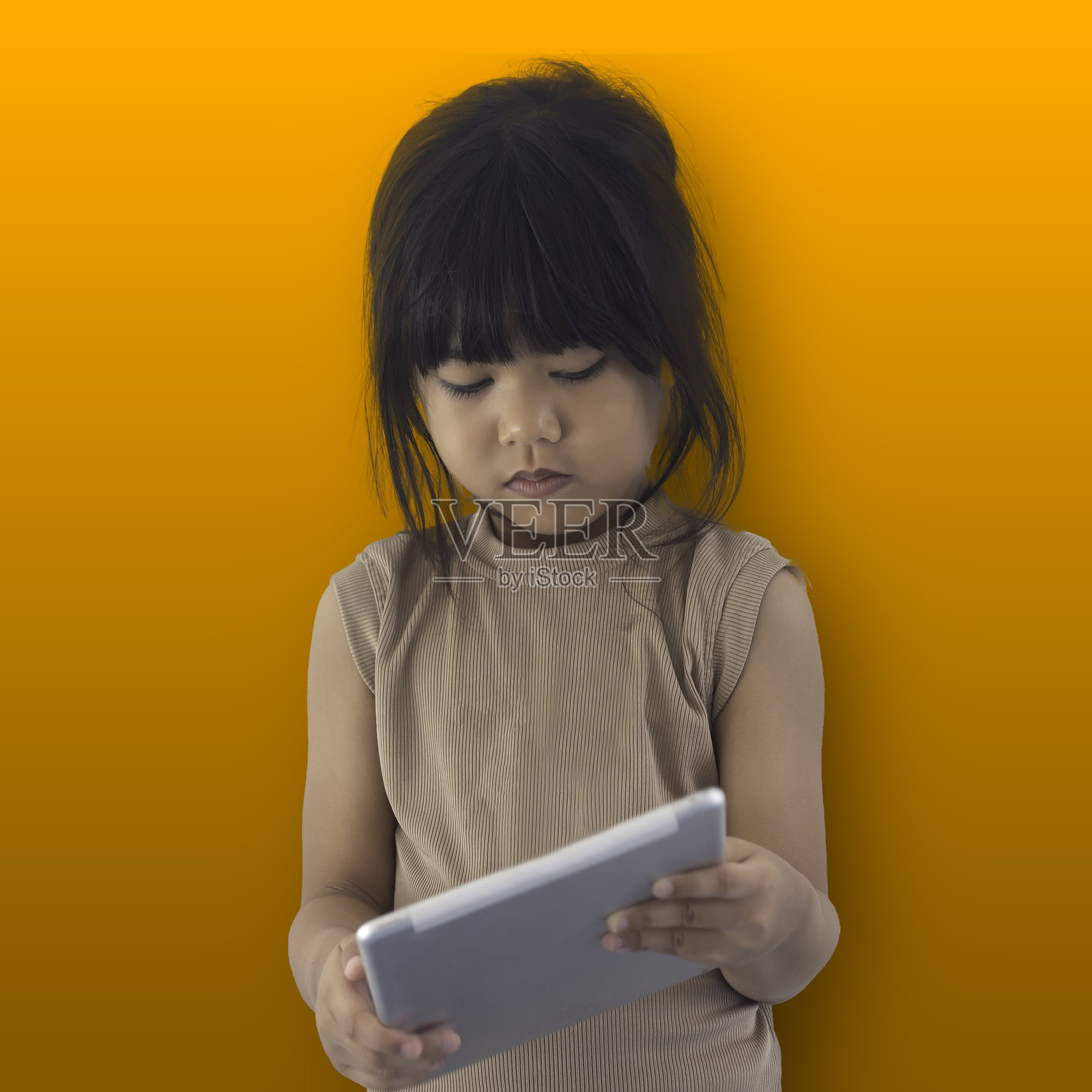 小女孩在橙色背景下拿着平板电脑。教育与科技概念。照片摄影图片