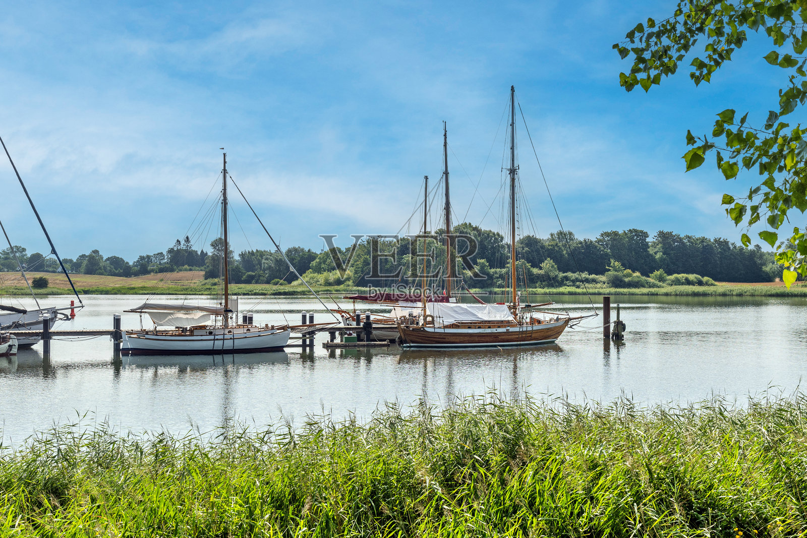 阳光明媚的日子里，小帆船停靠在河里。德国北部的施莱河。照片摄影图片