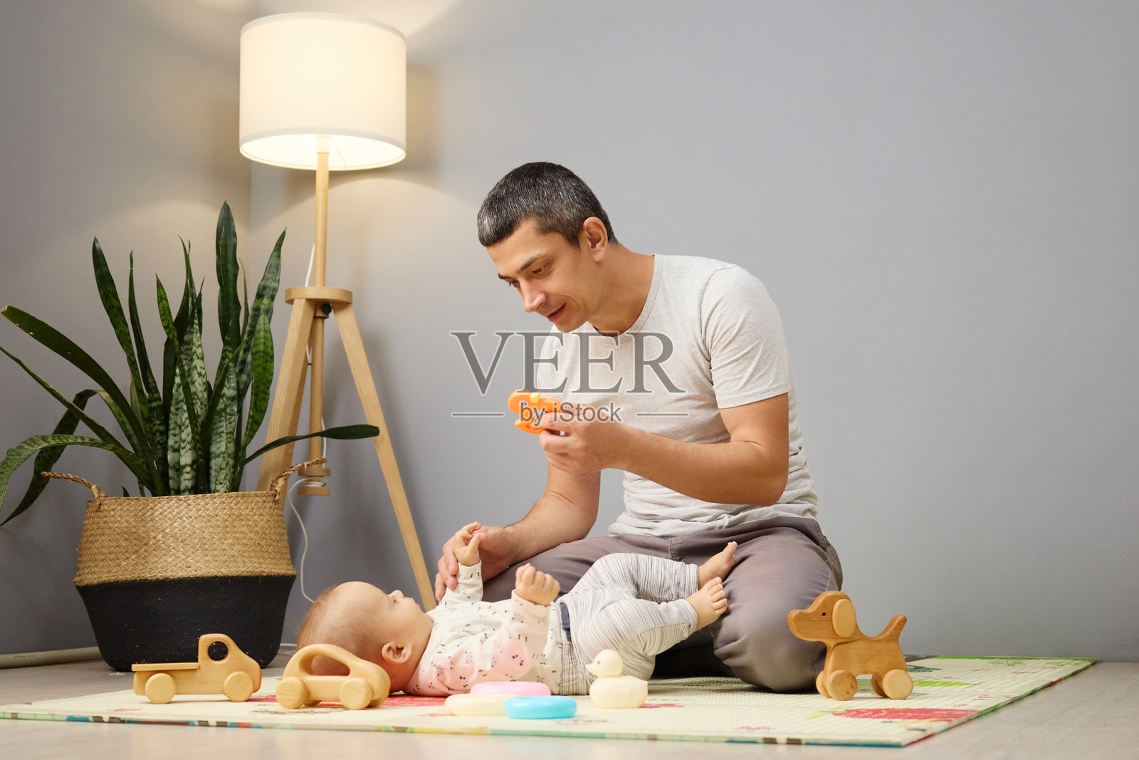 快乐的父亲坐在客厅的地板上，和他的小儿子一起玩玩具，享受着童年的乐趣和亲子间的亲密时光。照片摄影图片