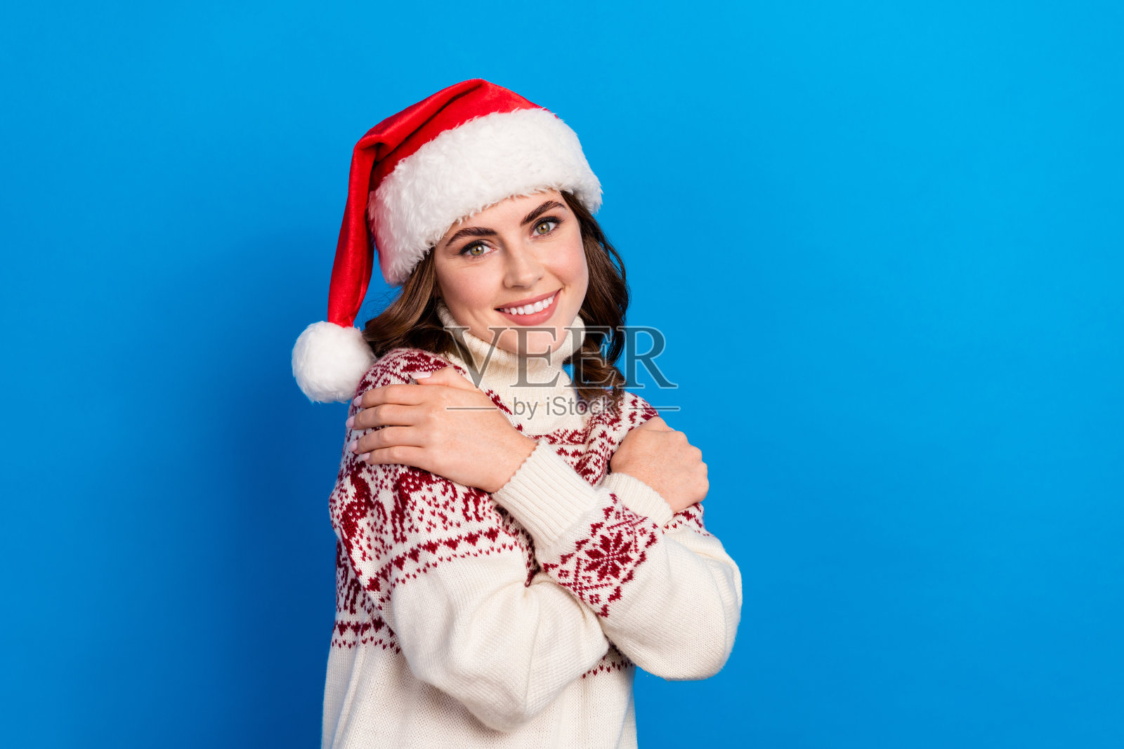 可爱的快乐女士穿着时尚的丑陋舒适毛衣，像高品质衣物一样拥抱自己，背景为蓝色。照片摄影图片