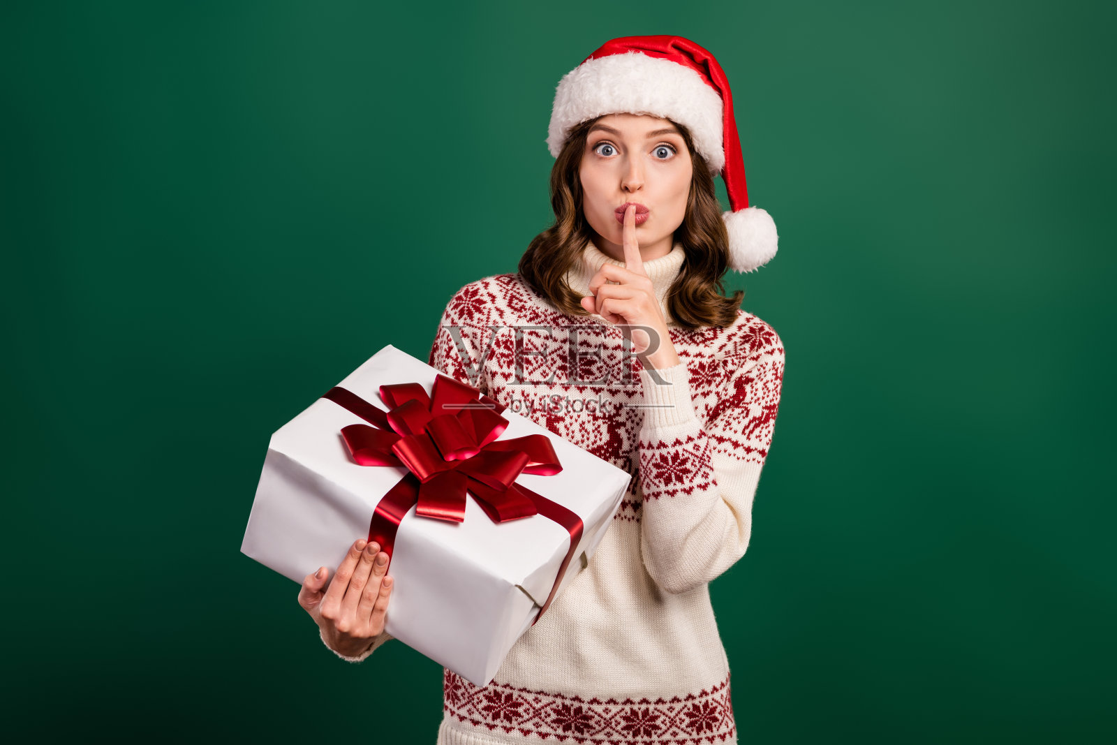 吸引人的人用手指触碰嘴唇做出嘘的手势，手里拿着礼盒，背景为绿色。照片摄影图片