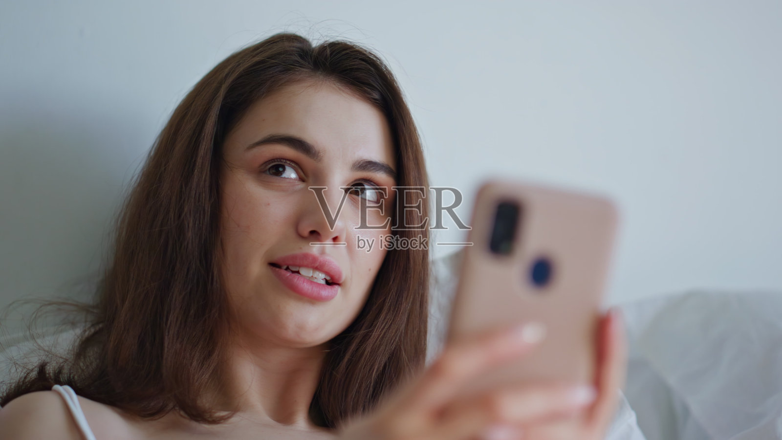 早晨的女孩在舒适的床上看手机，感到愉快，特写镜头。微笑的女人照片摄影图片