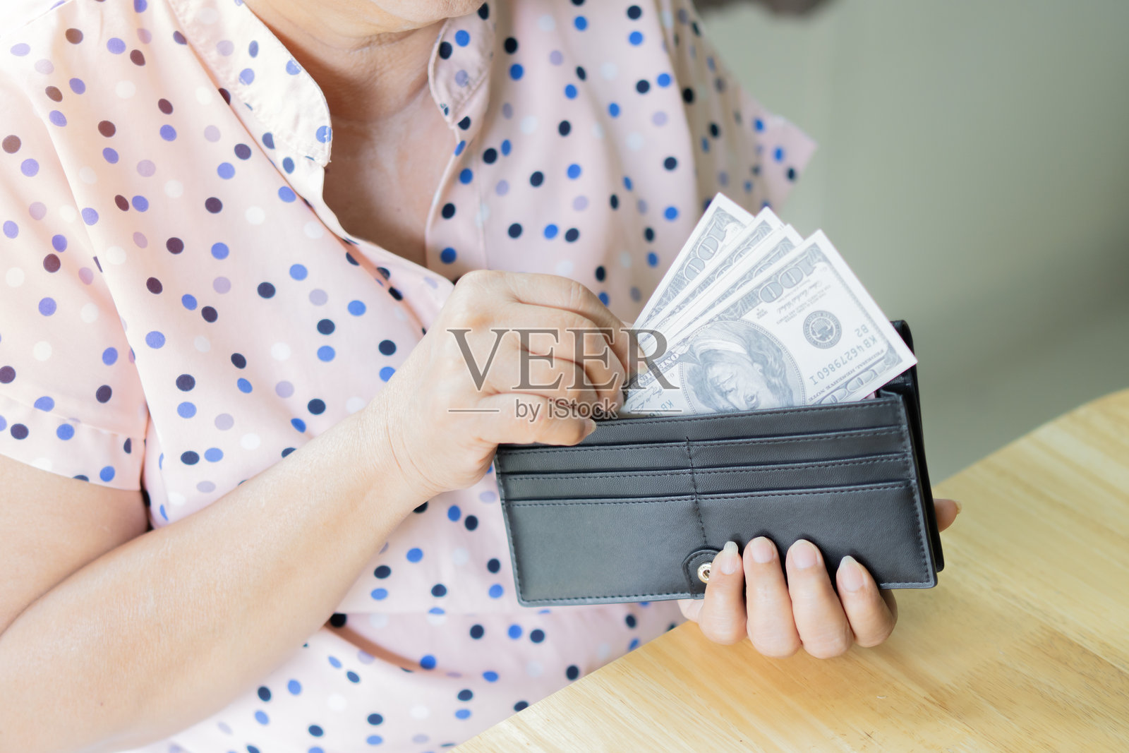 女人的手从黑色钱包中拿出美元钞票。老妇人在数钱。照片摄影图片