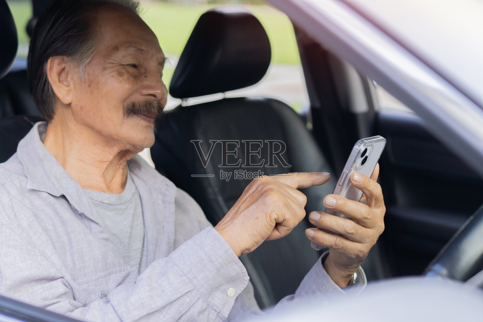 快乐的老年男子一手握着手机，一边开车使用智能手机照片摄影图片